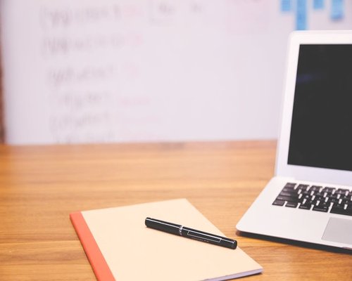 A notebook and pen on a desk beside a laptop